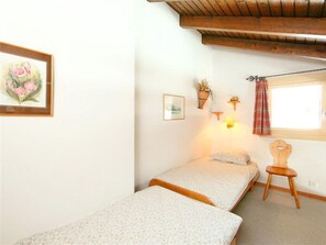 Un dormitorio pequeño con dos camas individuales, una silla de madera, una ventana con cortina y decoración en la pared.