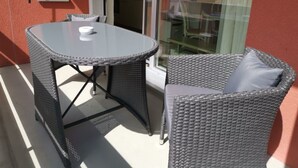 Uma varanda com porta de vidro, uma mesa de vime e um sofá de vime.
