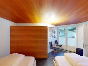 A room with two beds, a wooden wardrobe, a chair, and a door leading to a balcony. - Apartment Quadratscha by Interhome (Samedan)