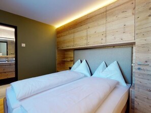 A double bed with white linens and a headboard against a wooden wall. - Apartment Quadrellas 3.5 by Interhome (Samedan)