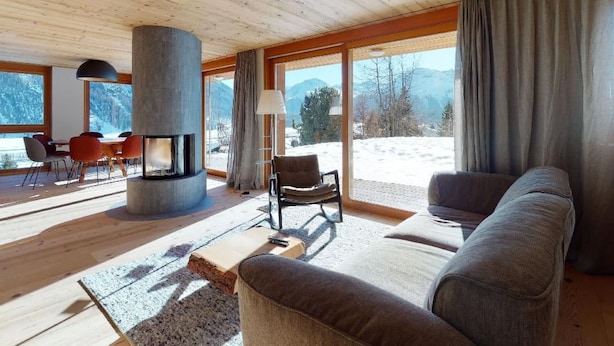 Un salón moderno con chimenea, ventanas grandes y vista a un paisaje nevado.