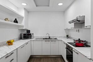 A modern kitchen with white cabinetry, a marble countertop, a built-in microwave, a stainless steel sink, and a red pot on the stove. - FIRST CLASS | 2BR | Luxury Retreat | Near Downtown (Business Bay)