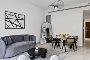 A modern living room with a grey sofa, a round coffee table, and a dining area with a white table and black chairs. - FIRST CLASS | 2BR | Luxury Retreat | Near Downtown (Business Bay)