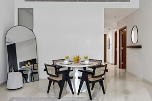 A modern dining area with a round table, four chairs, and a large mirror on the wall. - FIRST CLASS | 2BR | Luxury Retreat | Near Downtown (Business Bay)