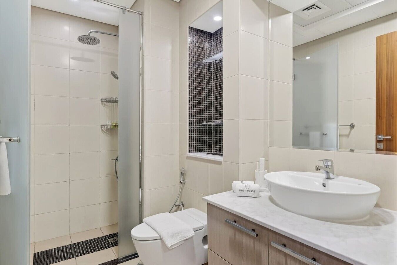 Een moderne badkamer met een douche met glazen wand, een grote spiegel en een wit wastafelmeubel.