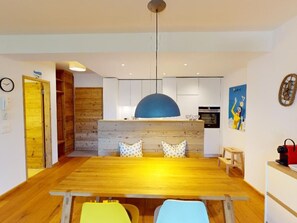 A modern kitchen with white cabinets, a blue pendant light, and a wooden dining table with chairs. - Apartment Sungold by Interhome (St. Moritz)