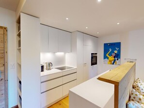 A modern kitchen with white cabinetry, a wooden countertop, and a poster on the wall. - Apartment Sungold by Interhome (St. Moritz)