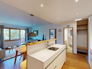A modern kitchen with a central island, a dining area with a table and chairs, and a view of the outdoors through large windows. - Apartment Sungold by Interhome (St. Moritz)