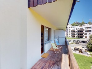Ein Balkon mit Holzboden, zwei gestreifte Lounge-Stühle und Blick auf ein Wohngebiet mit Gebäuden.