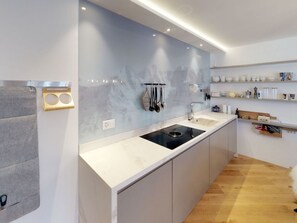 A modern kitchen with a marble backsplash, a built-in stove, and a wooden floor. - Apartment Di Roz by Interhome (St. Moritz)