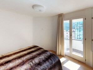 A room with a bed, a window with curtains, and a view of buildings outside. - Apartment Di Roz by Interhome (St. Moritz)