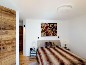 A bedroom with a bed, a wall-mounted artwork, bedside tables with lamps, and a wooden wardrobe. - Apartment Di Roz by Interhome (St. Moritz)