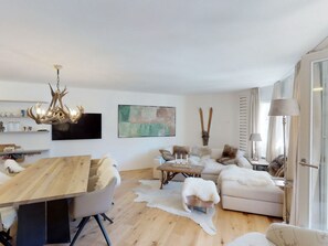 A modern living room with a wooden dining table, a sofa, a coffee table, and a chandelier. - Apartment Di Roz by Interhome (St. Moritz)