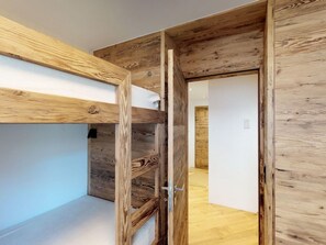 A room with a bunk bed, wooden walls, and a door leading to another room. - Apartment Di Roz by Interhome (St. Moritz)