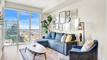 Una sala moderna con un sofá modular, una mesa de centro redonda y un amplio ventanal con vista a la ciudad.