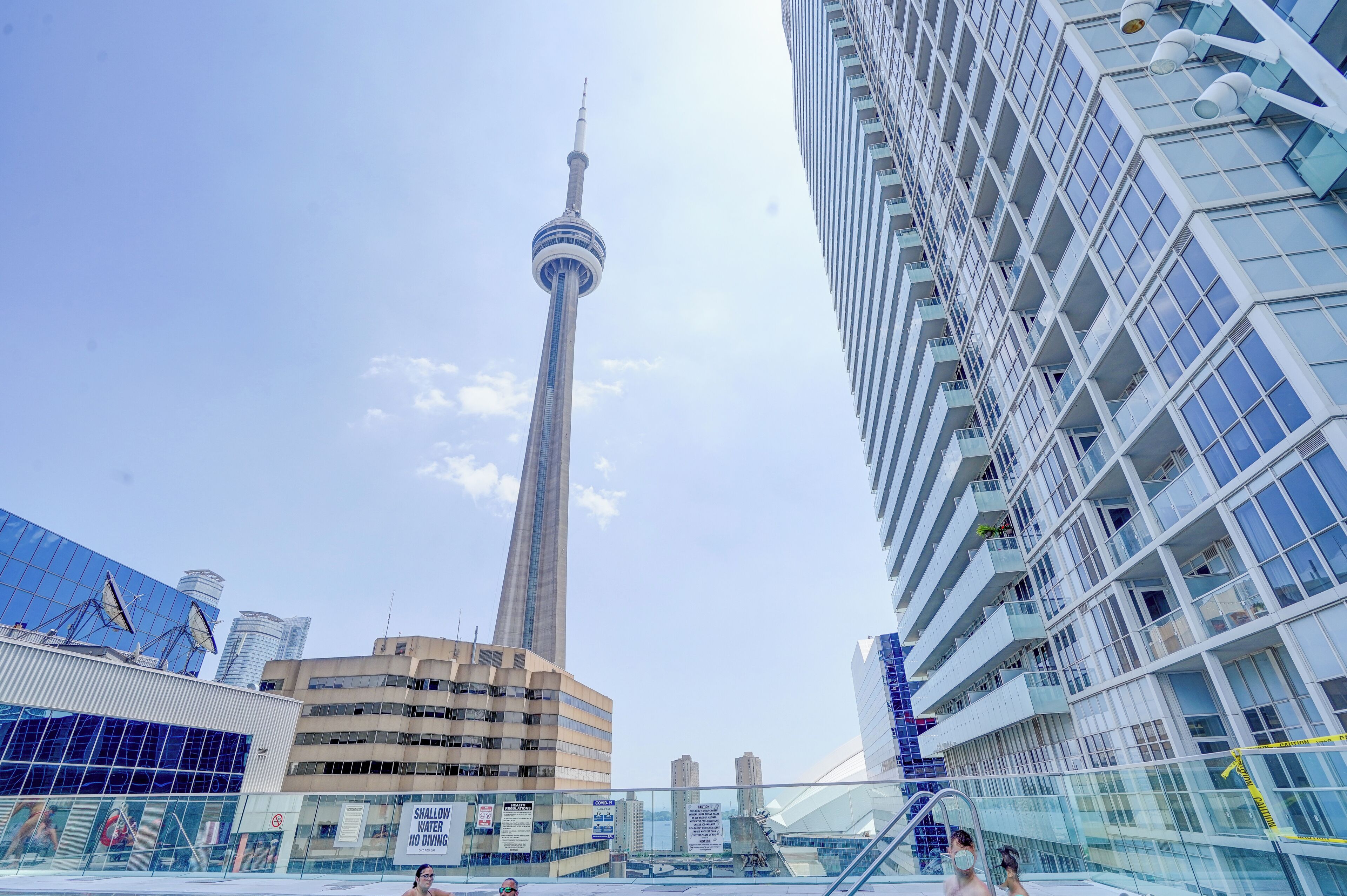 A modern building with a tower, a glass facade, and a sign indicating shallow water and no diving.