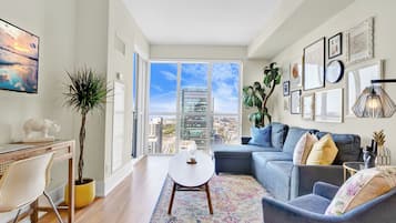 Una sala de estar moderna con un sofá, una mesa de centro, un escritorio y un amplio ventanal con vista a la ciudad.