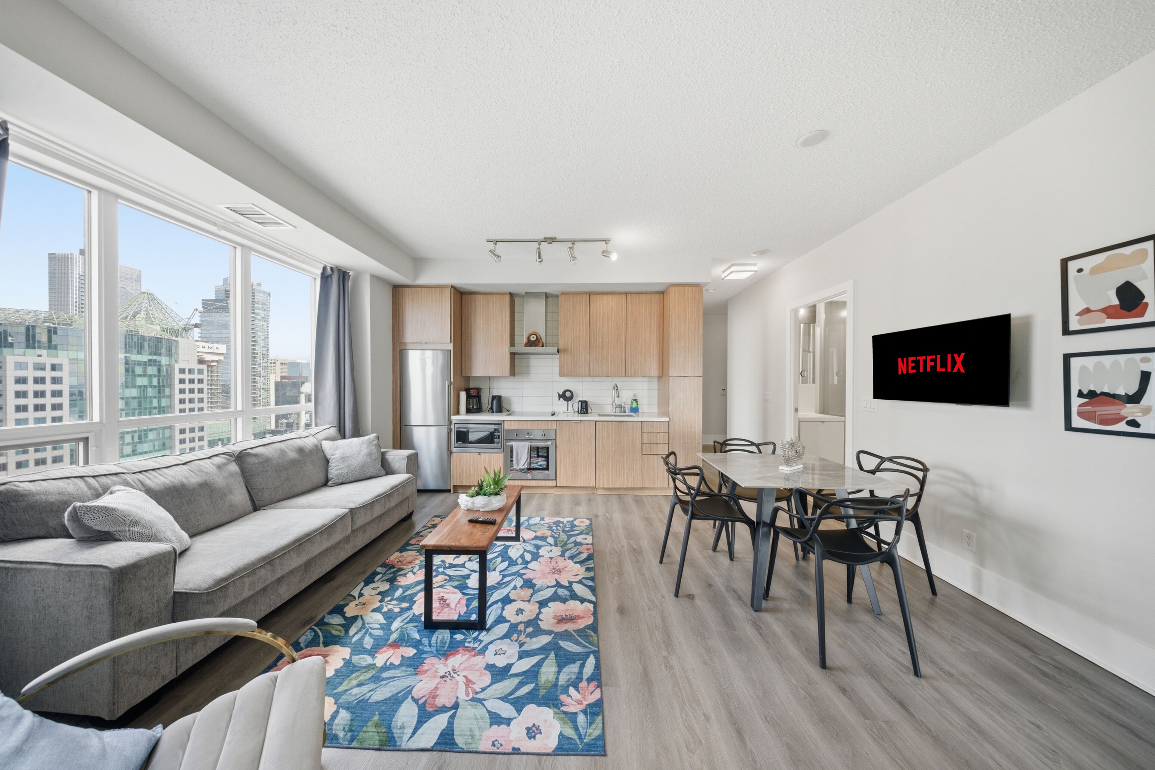 Um apartamento moderno com sala de estar, área de jantar, cozinha e uma grande janela com vista para a cidade.