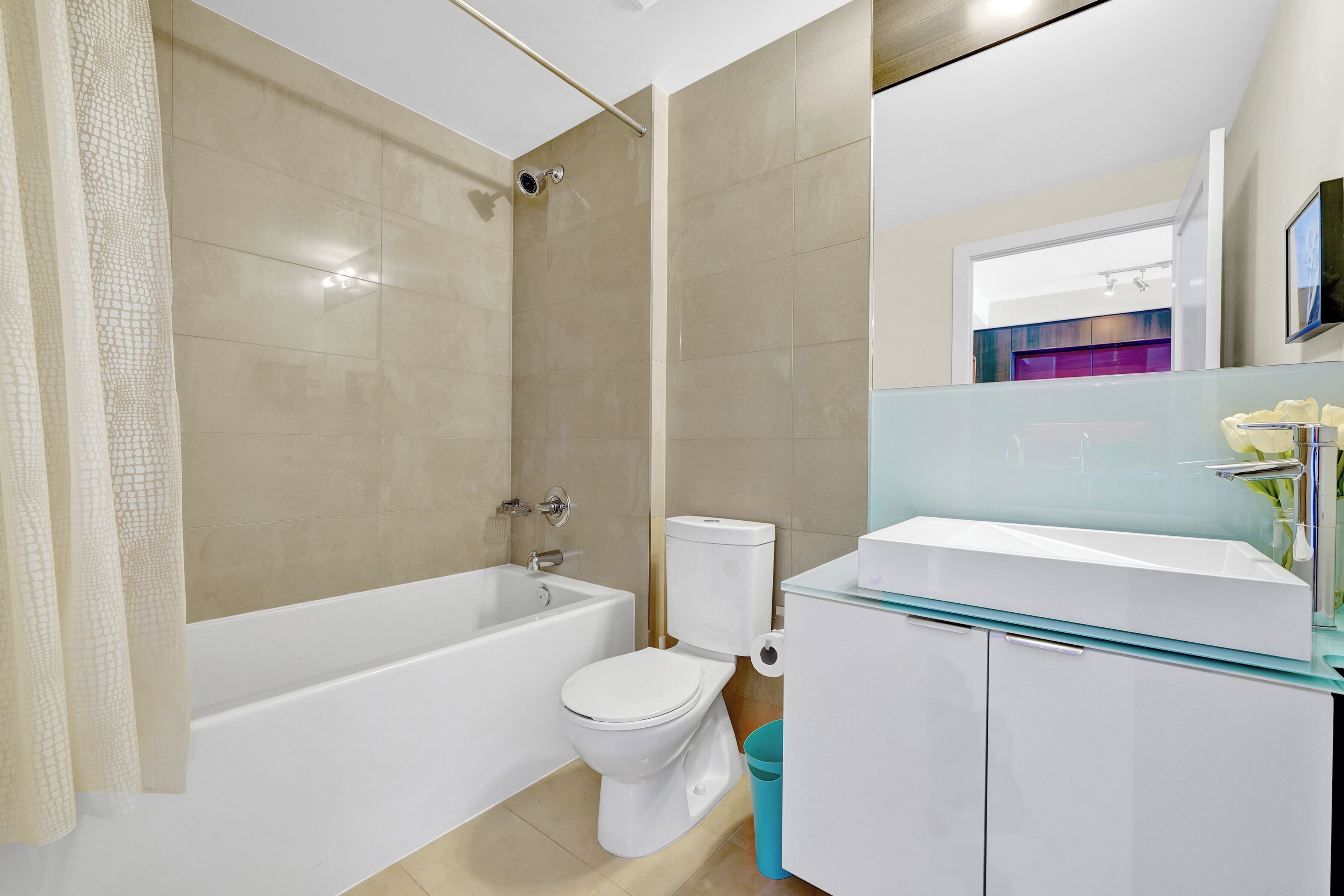 A modern bathroom with a bathtub, toilet, and glass-fronted sink.