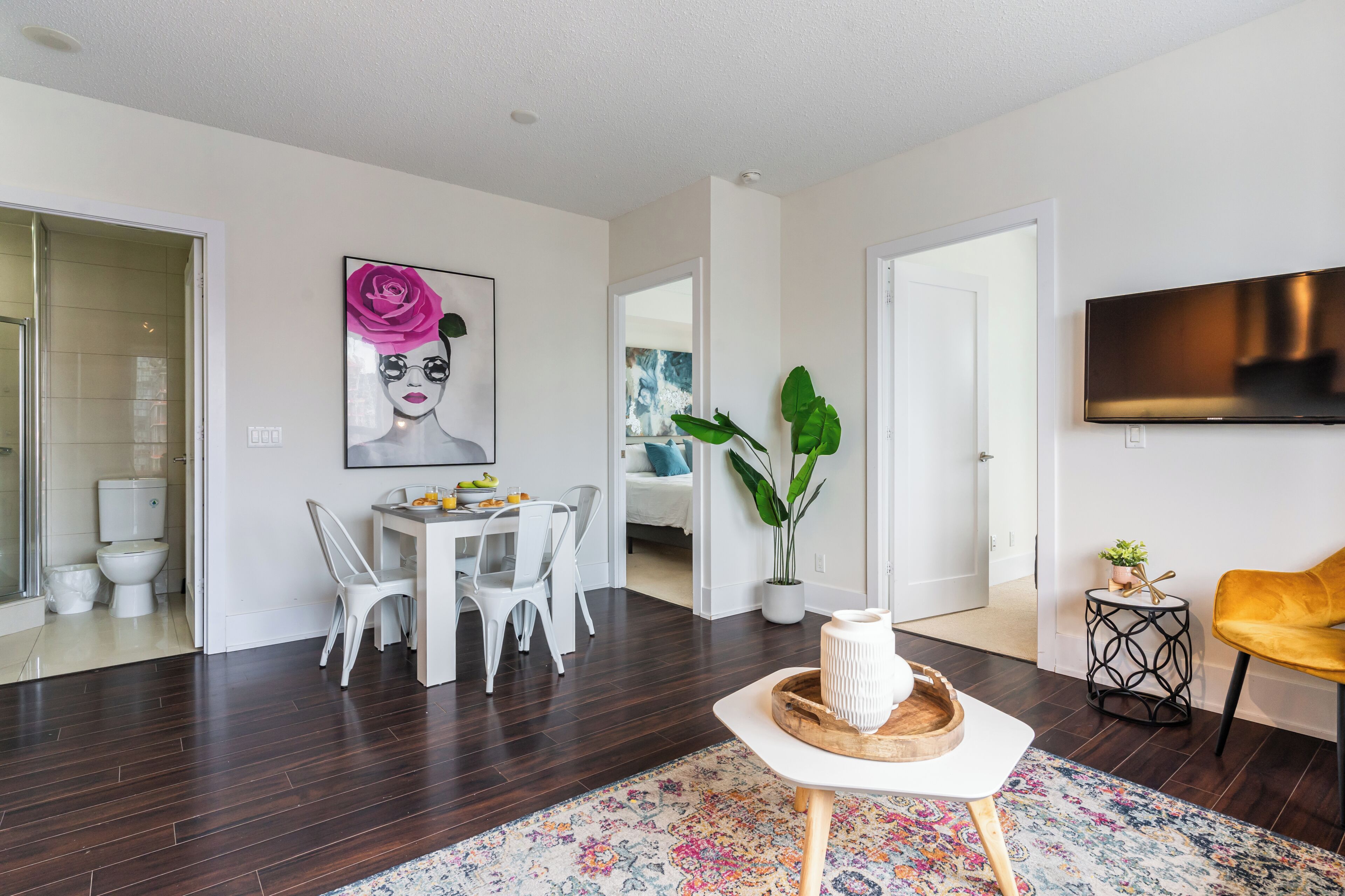 A modern living room with a dining area, a flat-screen TV, a potted plant, and a yellow chair.