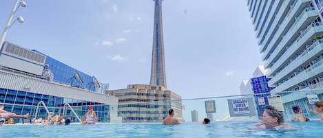A swimming pool with people, a tall tower in the background, and modern buildings.