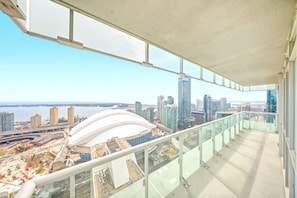 Un immeuble de grande hauteur doté d’un balcon en verre offrant une vue panoramique sur la ville, notamment sur un stade et divers autres bâtiments.