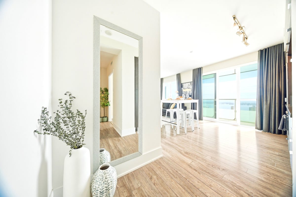 Una habitación de hotel moderna con un espejo grande, una zona de comedor con mesa y sillas, y un balcón con vistas.