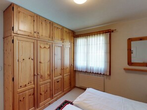 Une chambre avec des armoires en bois, un lit, une fenêtre avec des rideaux et un radiateur.