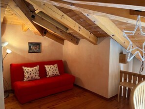 A red sofa with patterned cushions in a room with wooden beams and a star-shaped light fixture. - Apartment La Dmura by Interhome (Samedan)