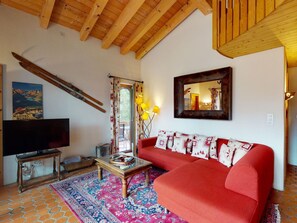 A living room with a red sofa, a wooden coffee table, a television, and a large mirror on the wall. - Apartment La Dmura by Interhome (Samedan)