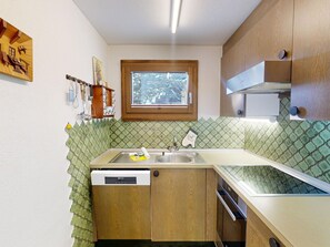 Eine kompakte Küche mit Holzschränken, einem integrierten Geschirrspüler, einem Fenster und einer gemusterten Spritzschutzwand.