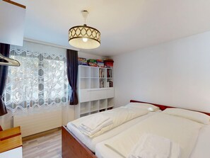 A hotel room with a bed, a wardrobe, a window with lace curtains, a bookshelf, and a hanging light fixture. - Apartment Piz Argient by Interhome (Samedan)