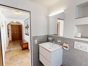 A modern bathroom with a white sink, grey tiles, a wooden door, and a mirror. - Apartment Piz Argient by Interhome (Samedan)