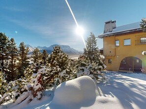 Schneebedeckte Landschaft mit einem Berg im Hintergrund, ein Gebäude mit gelber Fassade und strahlend blauem Himmel.