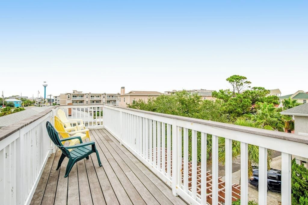 A wooden deck with a white railing, green and yellow chairs, and a view of residential buildings and greenery.