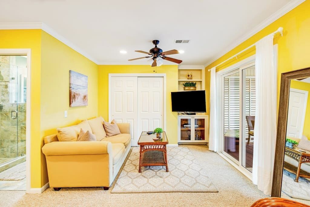 A living room with a sofa, a coffee table, a ceiling fan, a TV, and a sliding glass door.