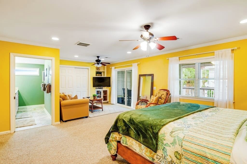 A bedroom with a bed, a ceiling fan, a window with curtains, and a door leading to another room.