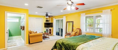 A bedroom with a bed, a ceiling fan, a window with curtains, and a door leading to another room.