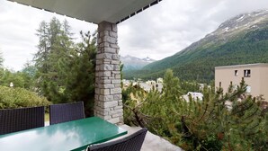 Un'area salotto esterna coperta con un pilastro in pietra, affacciata su un paesaggio montuoso con edifici in lontananza.