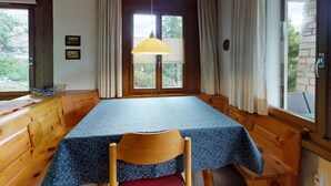 Una stanza con soffitto in legno, un tavolo con tovaglia blu, una sedia e una finestra con tende.