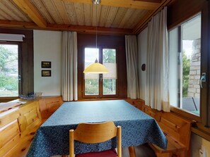 A room with a wooden ceiling, a table with a blue tablecloth, a chair, and a window with curtains. - Apartment Chavallera 36 by Interhome (St. Moritz)