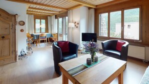 Un ampio soggiorno con soffitto in legno, un tavolo da pranzo, due divani, una TV e una grande finestra con vista sull'esterno.