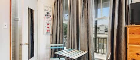 A room with a white door, a poster on the wall, a table with chairs, and a window with curtains.