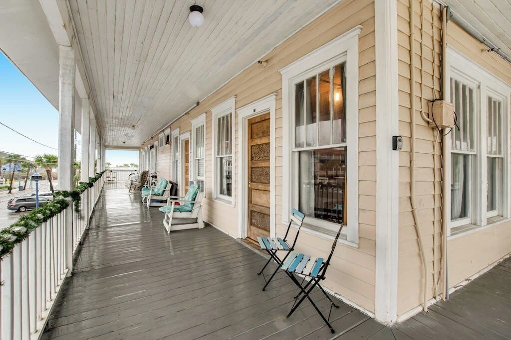 Une véranda avec une rangée de chaises et un banc, un plancher en bois et une balustrade blanche.