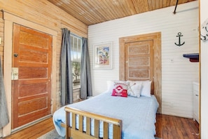 A wooden-paneled room with a bed, a door, and a wall-mounted anchor decoration. - Quaint 2nd-floor studio 1 block from the beach with fast WiFi, deck, cable, & AC (Tybee Island)
