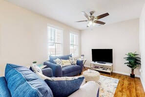 A living room with a sofa set, a television, a ceiling fan, and a plant. - Renovated bungalow with central AC, W/D, & modern kitchen, Free Wifi (Savannah)