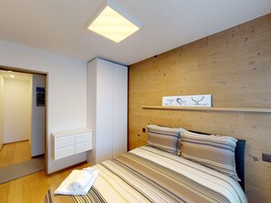 A modern bedroom with a bed, a wooden headboard, a bedside table, and a wall-mounted artwork. - Apartment Allod 210 by Interhome (St. Moritz)