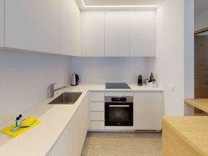 A modern kitchen with white cabinetry, a stainless steel sink, a built-in oven, and a countertop with a kettle and a bottle. - Apartment Allod 210 by Interhome (St. Moritz)