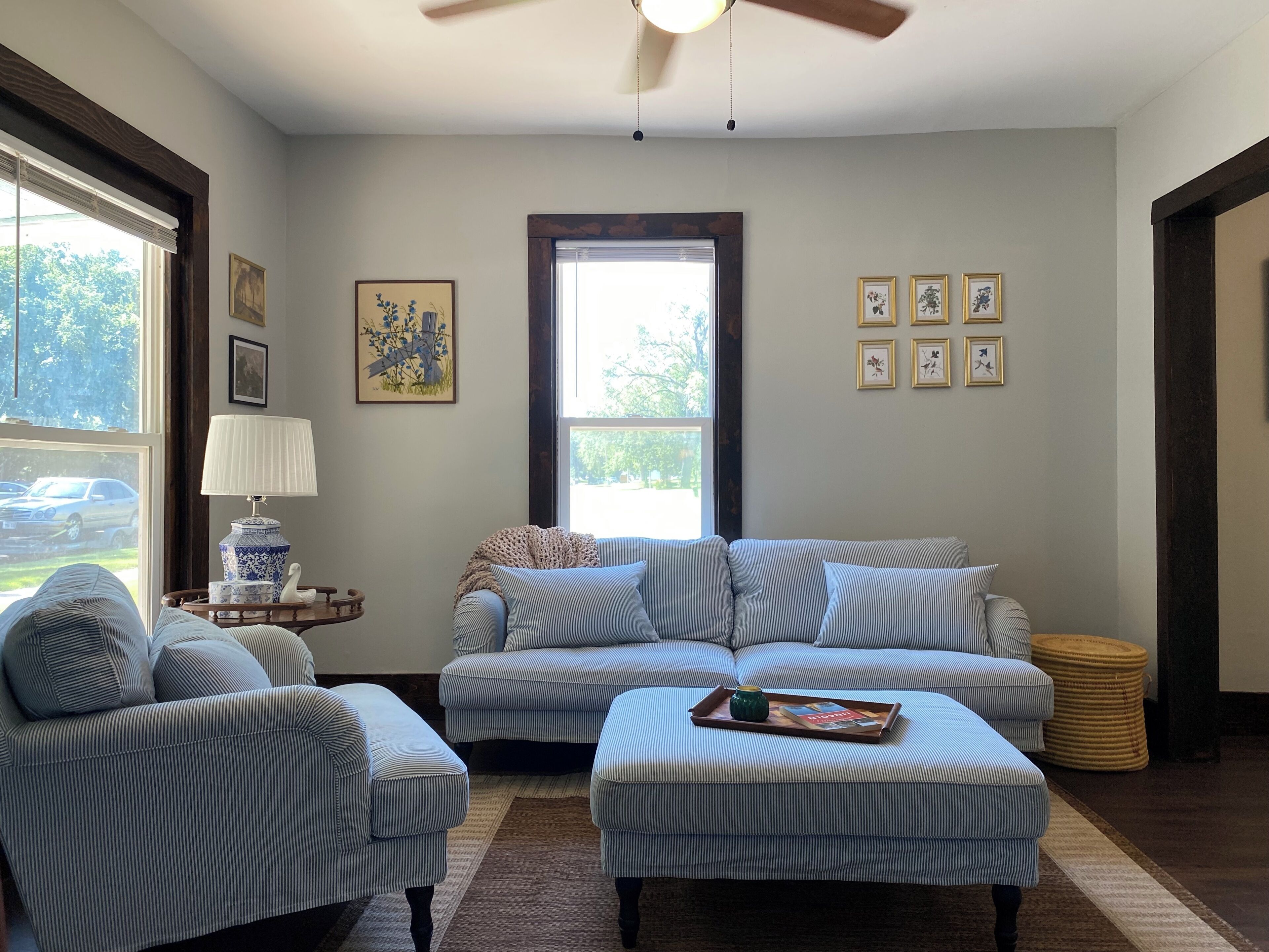 A living room with a sofa, armchair, and ottoman, a lamp, and framed pictures on the wall.