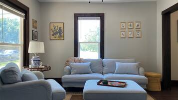 A living room with a sofa, armchair, and ottoman, a lamp, and framed pictures on the wall.